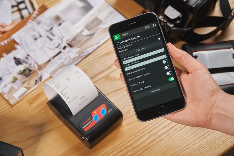 Telefon s pokladní aplikací vedle přenosné účtenkové tiskárny s vytištěným dokladem.